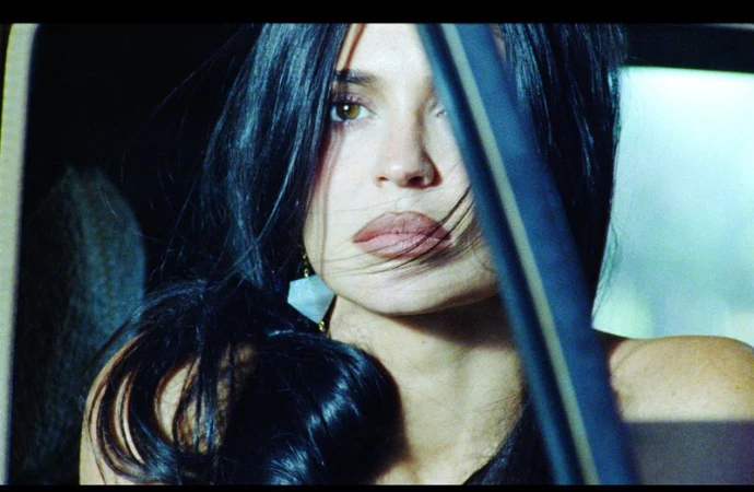 Close-up portrait of Kylie Jenner looking forward from inside a car with dark hair swept across her face.