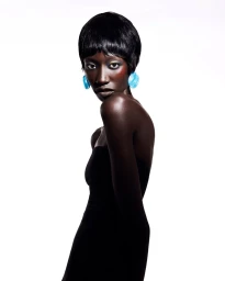Black woman with short black hair wearing a strapless black top and bright blue statement earrings against a white backdrop.