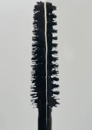 Macro close-up of a black textured mascara wand and bristles against a plain light neutral backdrop.