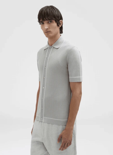 Portrait of a man in a light grey button-down short-sleeve shirt with white trim and light grey pants against a white backdrop.
