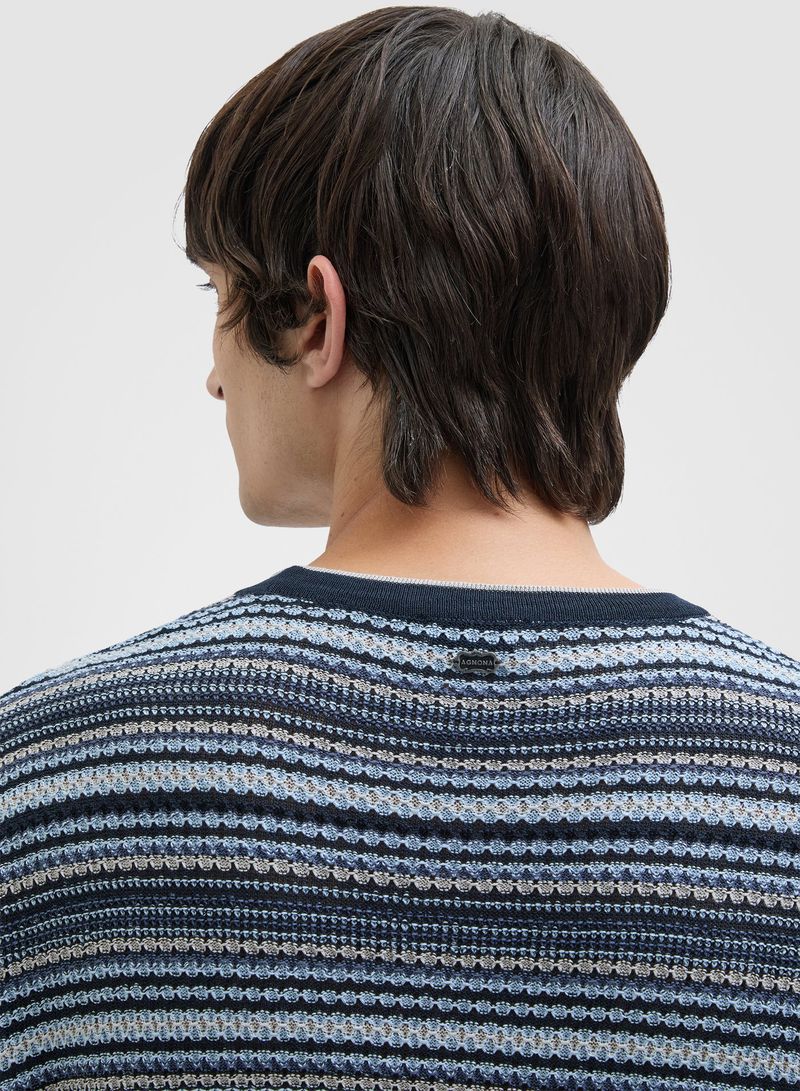 Back view of a person with dark hair wearing a striped knit sweater with shades of blue and grey against a neutral background.