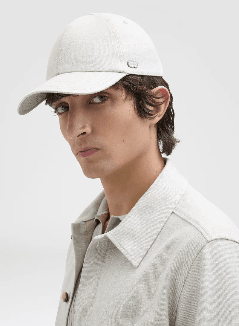 Close-up shot of a young adult man wearing a light gray baseball cap and matching shirt against a white background in a studio setting.