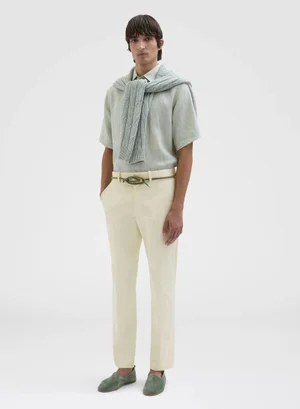 Male model in short-sleeved light shirt, cream trousers, and draped knit sweater against a white seamless background