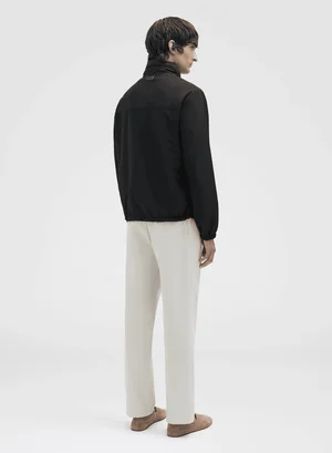 Rear view of male model wearing a dark jacket and light trousers against a neutral background for Agnona Spring Summer 2025.