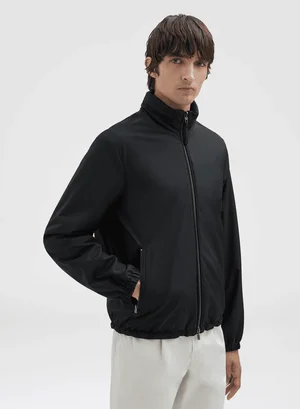 Model wearing a black zip jacket and light trousers against a neutral white background for Agnona spring summer 2025.