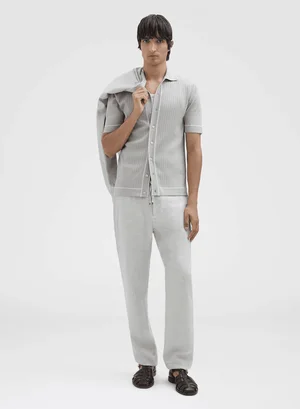 Male model wearing grey knit short-sleeve button-down shirt and trousers holding jacket over shoulder