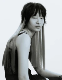 East Asian model with a textured two-tone mullet and long straight hair extensions posing in black strapped apparel against a white backdrop.