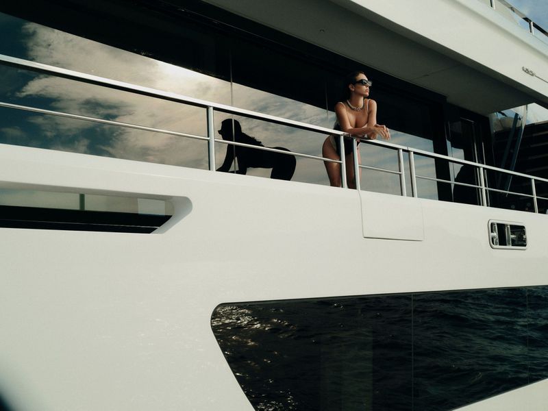 Georgina Rodriguez wearing sunglasses and a black swimsuit while leaning against the railing of a white luxury yacht.