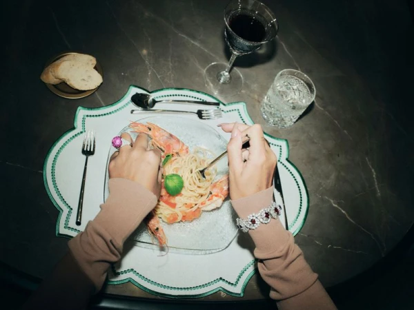 Georgina Rodriguez wearing a luxury diamond ruby bracelet and cocktail ring while eating prawn pasta at a dark marble table.