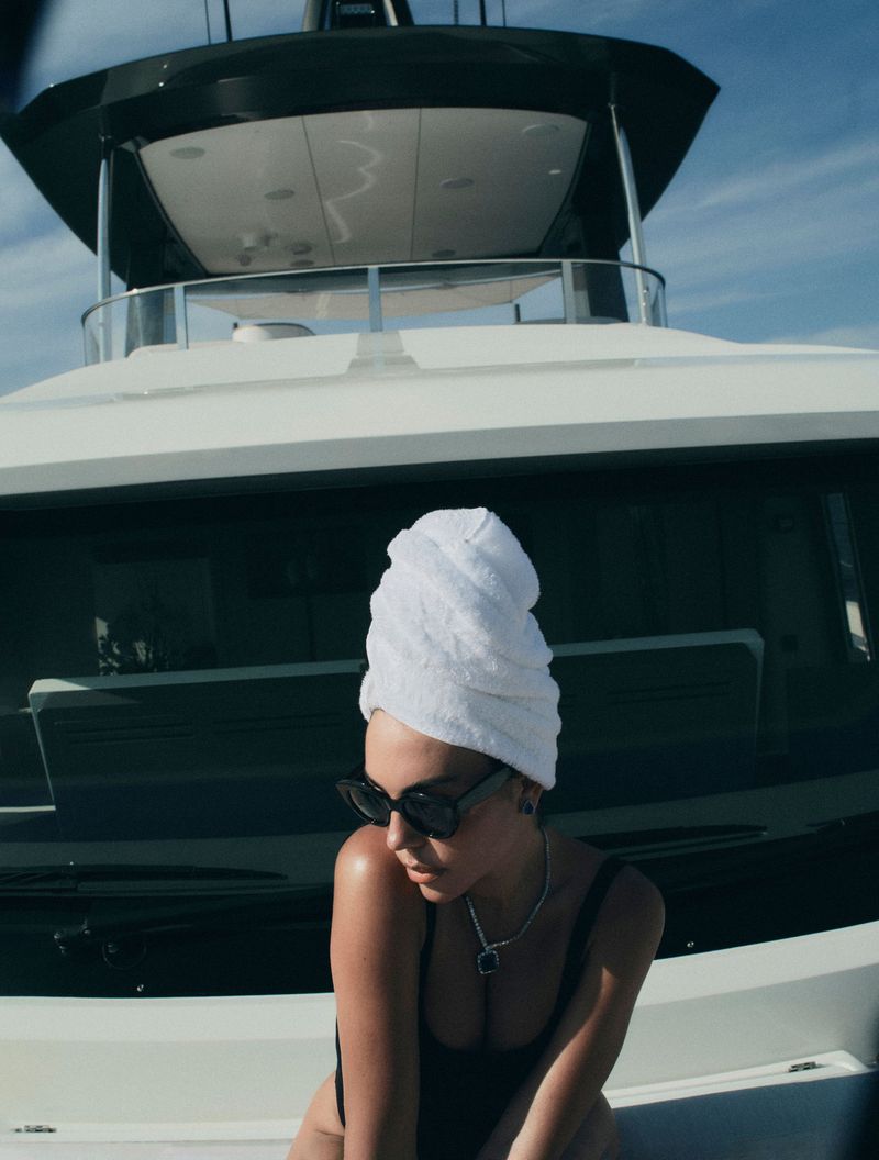 Georgina Rodriguez wearing a white head towel, dark sunglasses, and black swimwear aboard a luxury yacht.