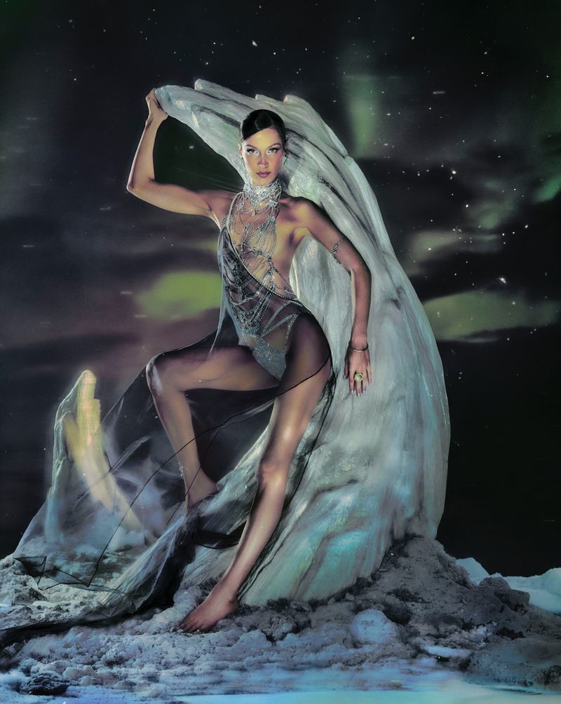A woman poses in a sheer gown with an updo hairstyle next to a large shell against a cosmic dark sky for a fashion photoshoot.