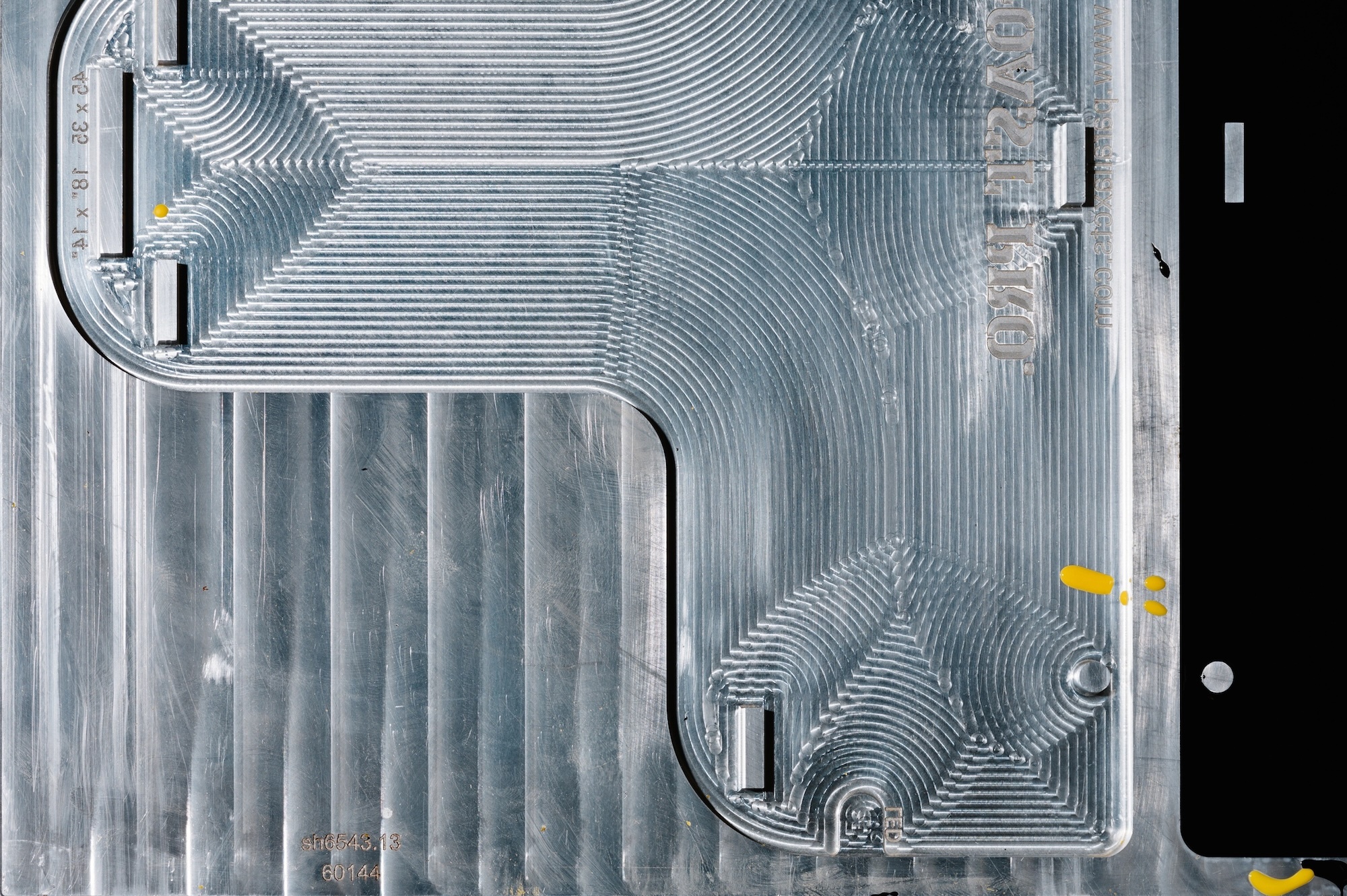 Top-down view of a precision-machined aluminum plate with intricate CNC milling toolpaths and engraved industrial markings.
