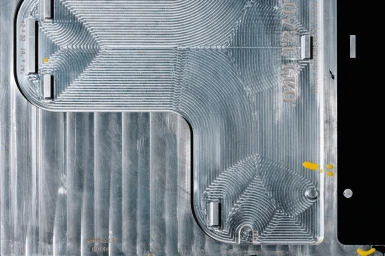 Top-down view of a precision-machined aluminum plate with intricate CNC milling toolpaths and engraved industrial markings.