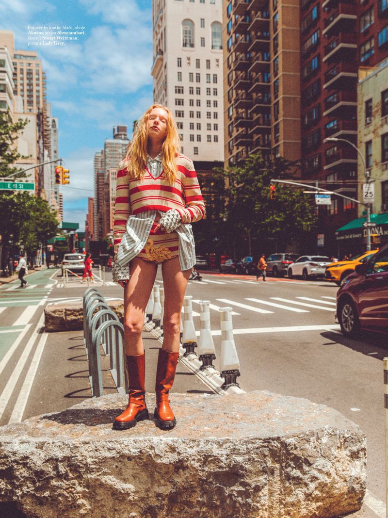 Fashion editorial shot in urban setting with a female model wearing a striped sweater, shorts, and knee-high boots on a city street.