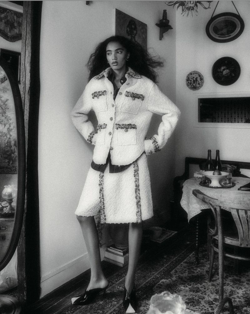 Model Noa Kaiser posing in a light tweed skirt suit inside a vintage room in black and white.