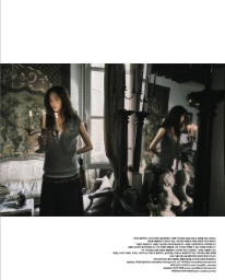 Model holding a candelabra with lit candles in an ornate vintage room beside an antique mirror reflecting her figure.