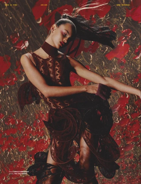 Fashion editorial shot of a female fashion model with dark hair wearing a patterned dress, choker, and wristband against a floral backdrop.