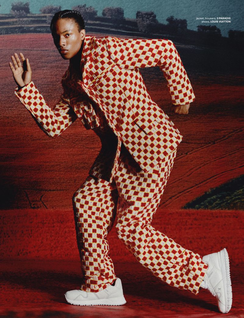 A person in a red-and-white checkered suit and white sneakers is captured in motion against a soft, painterly backdrop.