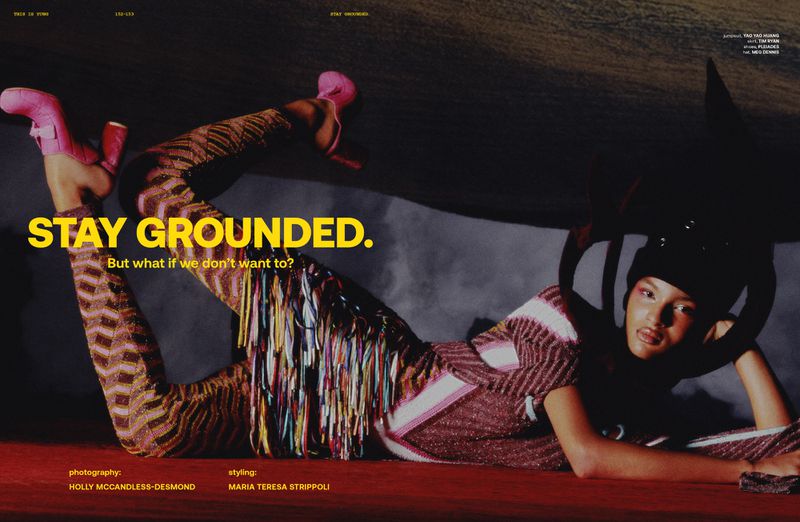 Fashion editorial shot of an adult woman lying on a red surface wearing patterned knitwear and pink boots in a studio environment.