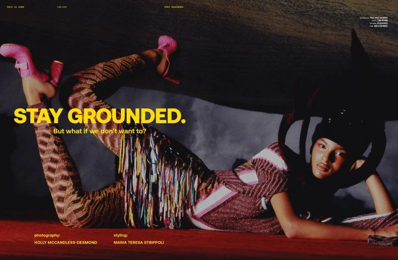 Fashion editorial shot of an adult woman lying on a red surface wearing patterned knitwear and pink boots in a studio environment.