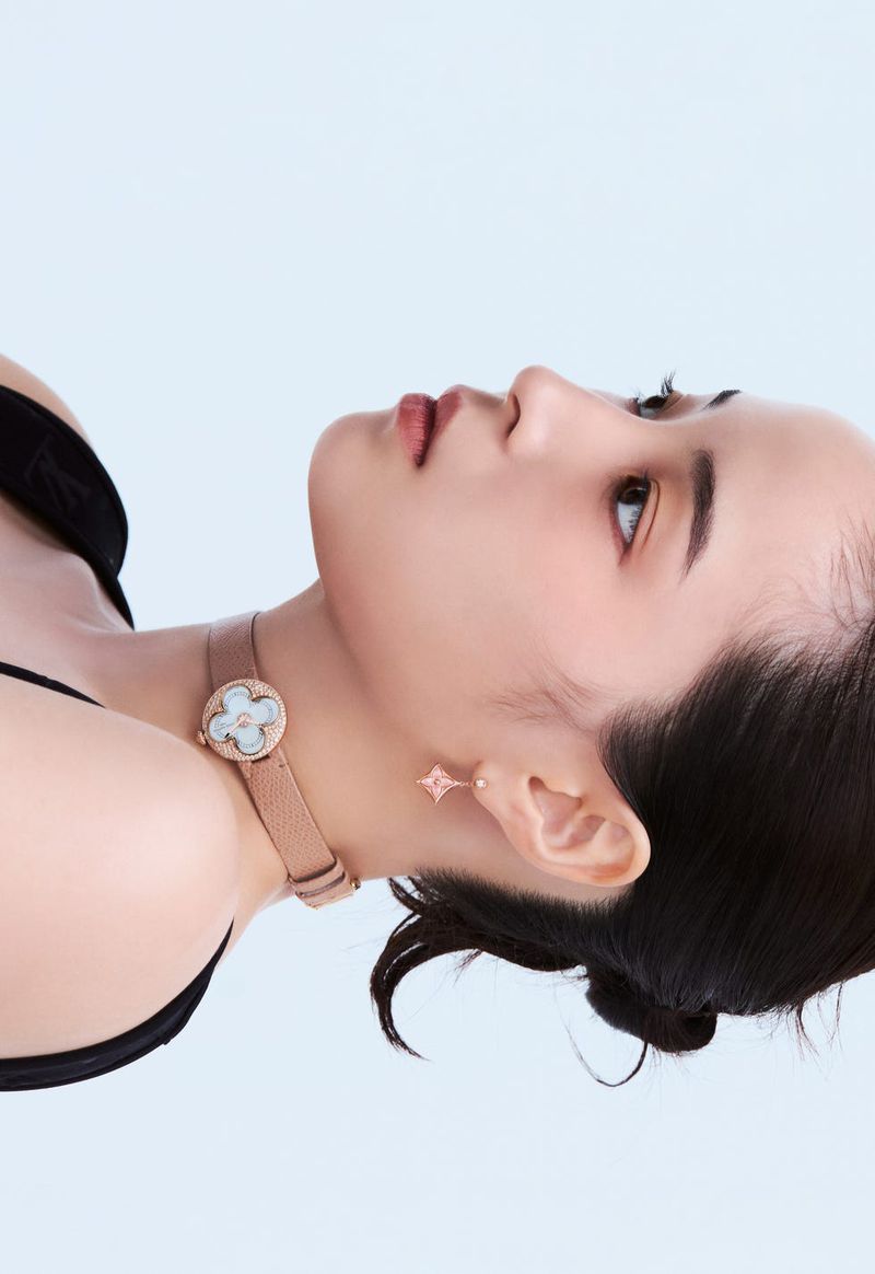 Profile view of Japanese actress Suzu Hirose wearing a leather choker watch and drop earring against a pale studio backdrop.