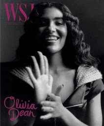 Black and white portrait of Olivia Dean smiling with hands raised, wearing a zipped top and knit collar for WSJ. Magazine.