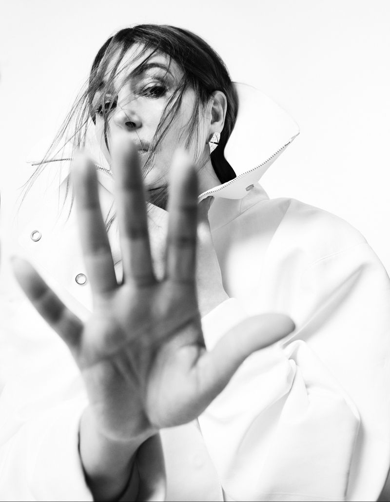 Monochrome portrait of an adult woman with her hand outstretched toward the camera in a white shirt with a large collar.