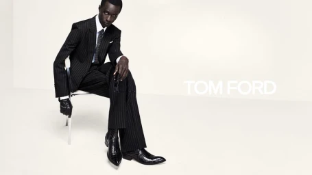 Model Malick Bodian seated in a black pinstripe suit and textured leather boots against a white studio background for Tom Ford.