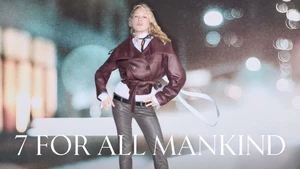 Chloë Sevigny posing in a burgundy leather jacket and dark patterned trousers for 7 For All Mankind against blurred night city lights.