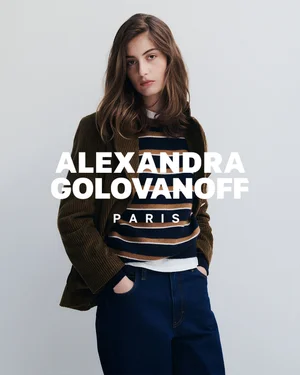 Model wearing a brown corduroy jacket, striped knit sweater, and dark jeans against a neutral studio backdrop.