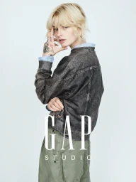 Esther Rose McGregor posing in a washed black denim jacket and sage green trousers against a pale studio background for Gap Studio.