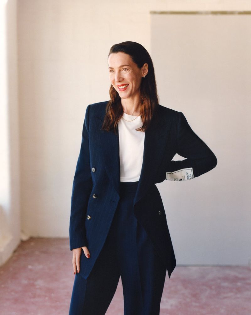 Stylish adult woman in a navy blue suit and white t-shirt poses in a minimalist indoor setting with natural light, looking away.