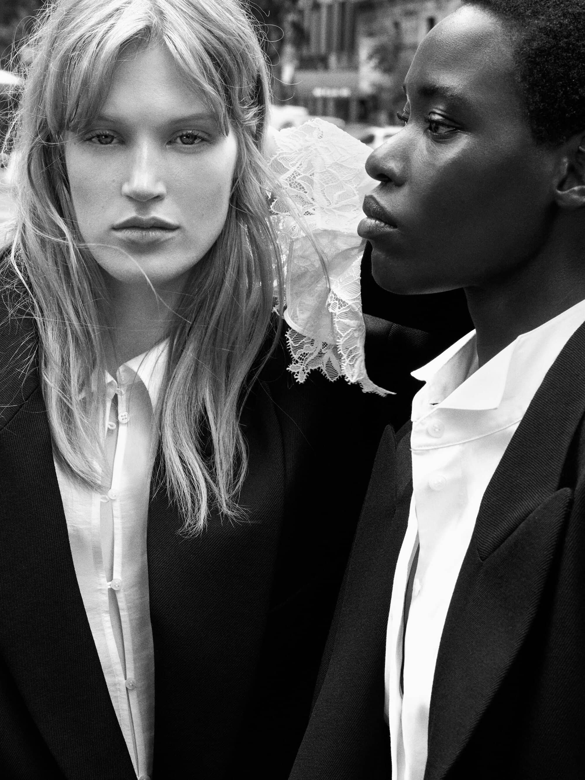 Two models posing closely outdoors in tailored black blazers and collared white shirts in black and white.