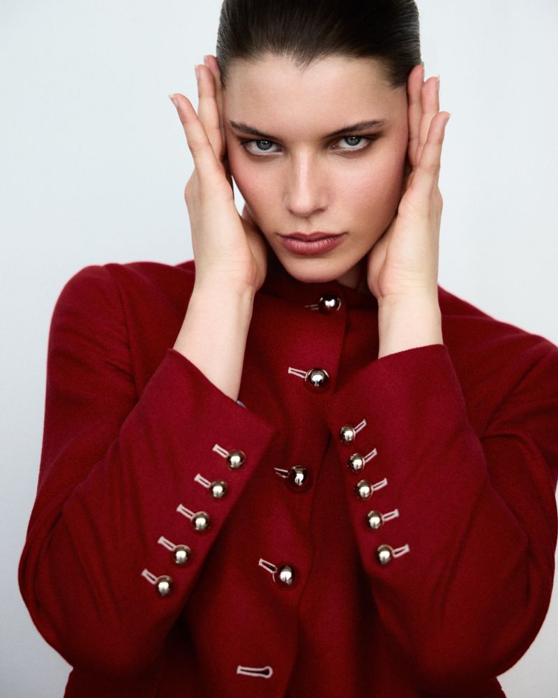 Model Mirthe Dijk poses in a red tailored jacket with silver sphere buttons against a clean white backdrop.