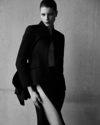 Mirthe Dijk wearing a black structured blazer and high slit skirt against a textured studio wall.