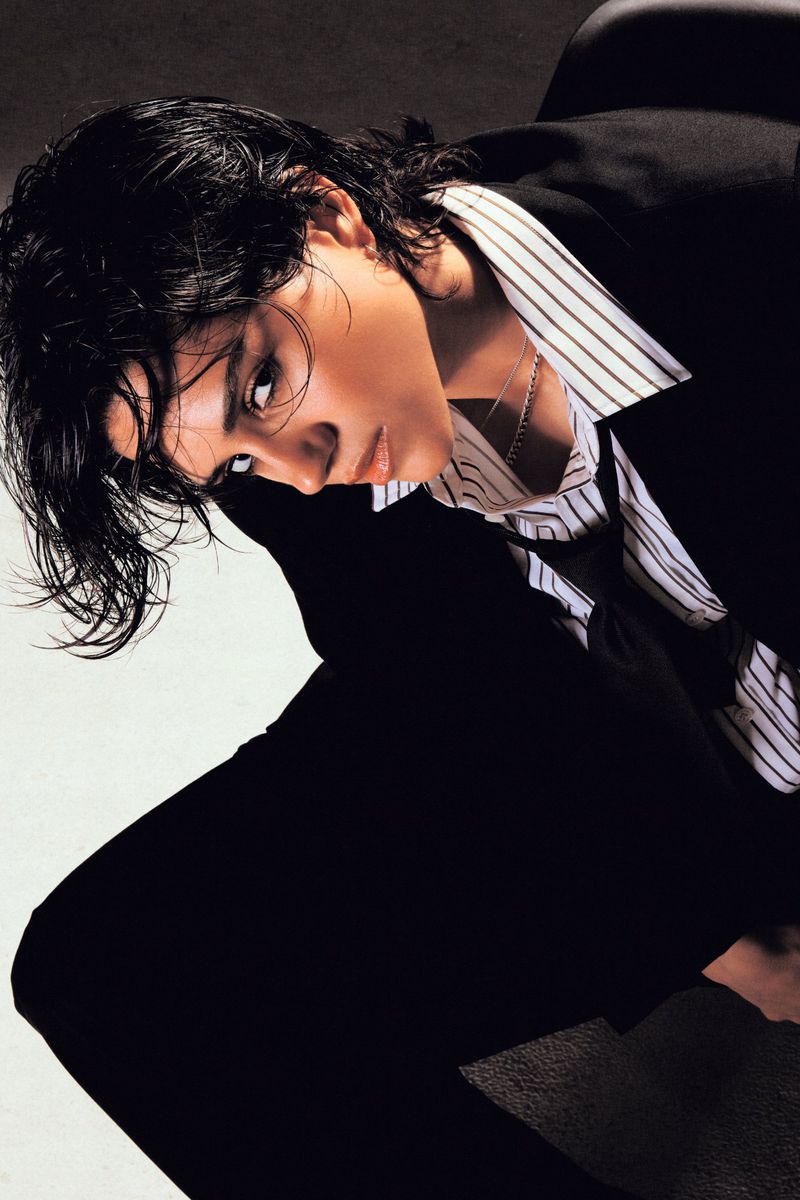 Sasha Calle posing in an oversized black suit and striped collared shirt with wet-look hair for Numéro Netherlands.
