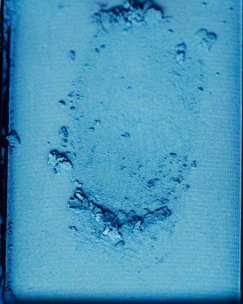 Macro close-up of vibrant blue pressed cosmetic powder with a crumbled circular imprint in a makeup pan.