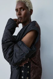 Model Amanda Parker in a modular black quilted garment with lace-up side detailing against a neutral backdrop.