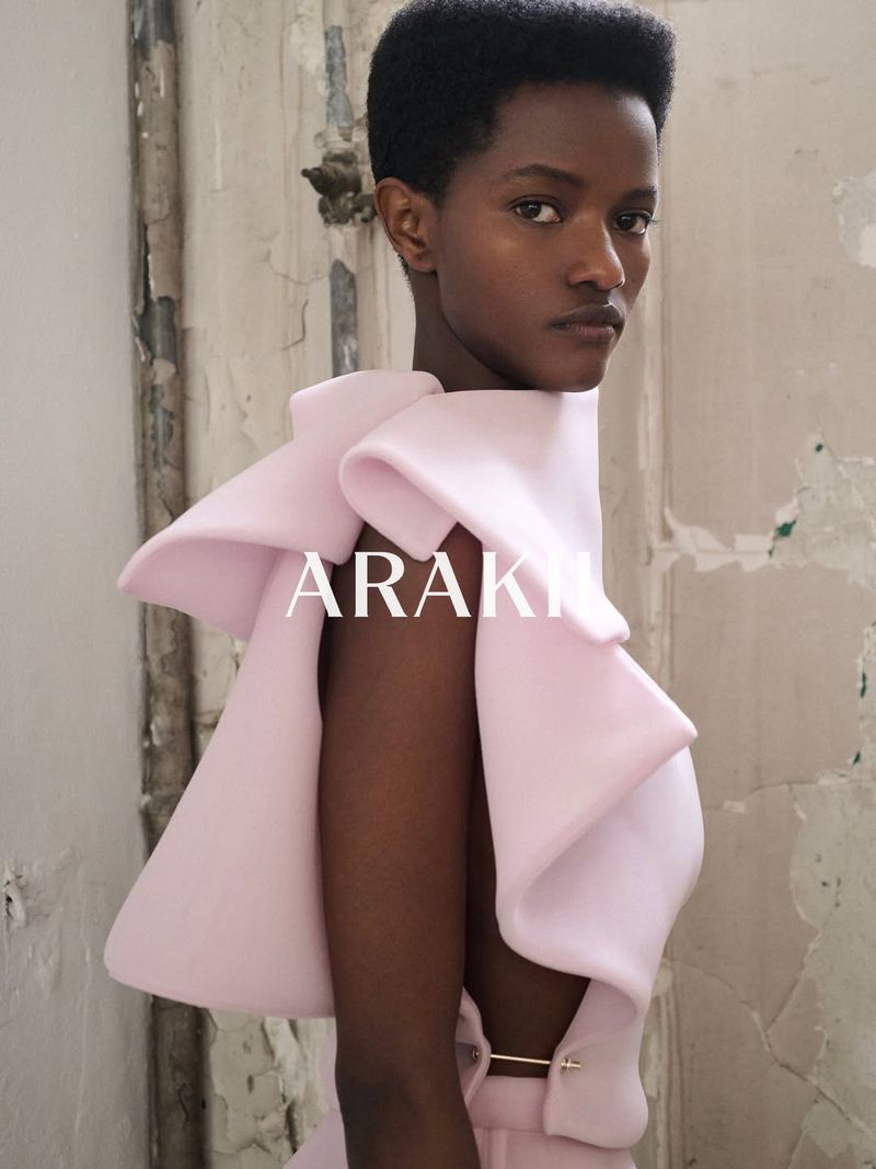 Model Anipha Umufite wearing a structural blush pink top against a distressed wall in the ARAKII Summer 2026 campaign.