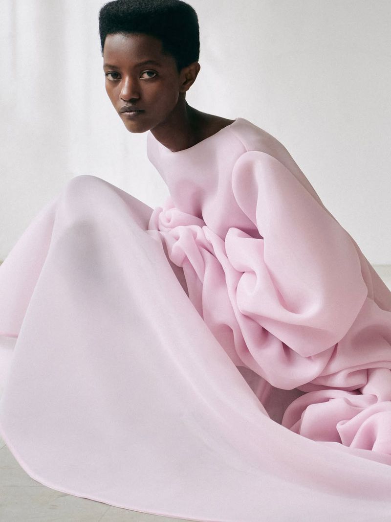 Model Anipha Umufite wearing a voluminous light pink sculptural gown against a bright studio backdrop.
