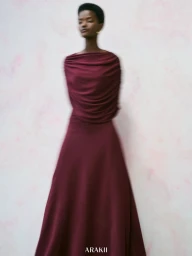 Model Anipha Umufite in a draped burgundy maxi dress posing against a soft textured background for ARAKII.