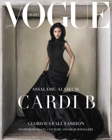 Cardi B wearing a dramatic black high-neck gown with a voluminous skirt inside a recessed neutral alcove for Vogue Arabia.