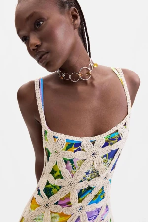 Black female model wearing a cream floral crochet dress layered over a colorful print against a white studio background.