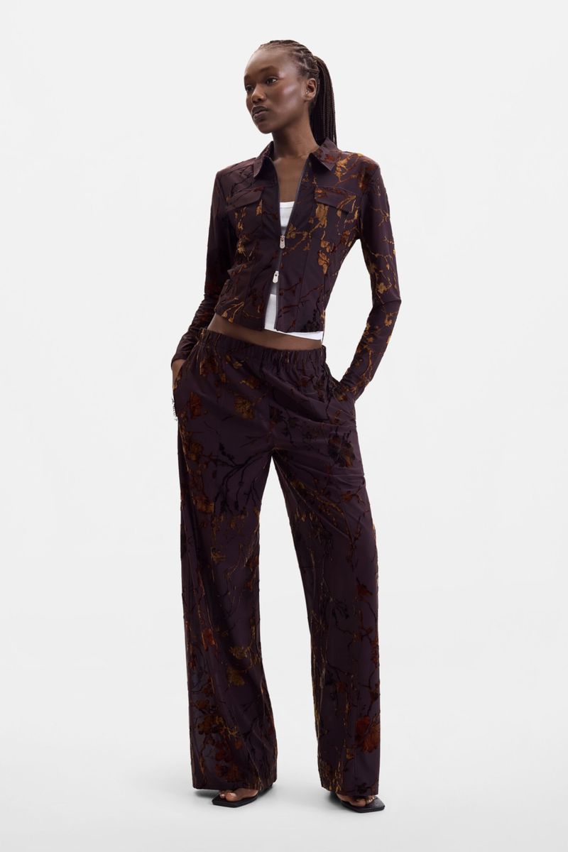 Black female model wearing a dark brown patterned long-sleeve shirt and matching wide-leg trousers against a white background.