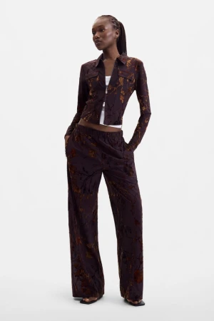 Black female model wearing a dark brown patterned long-sleeve shirt and matching wide-leg trousers against a white background.