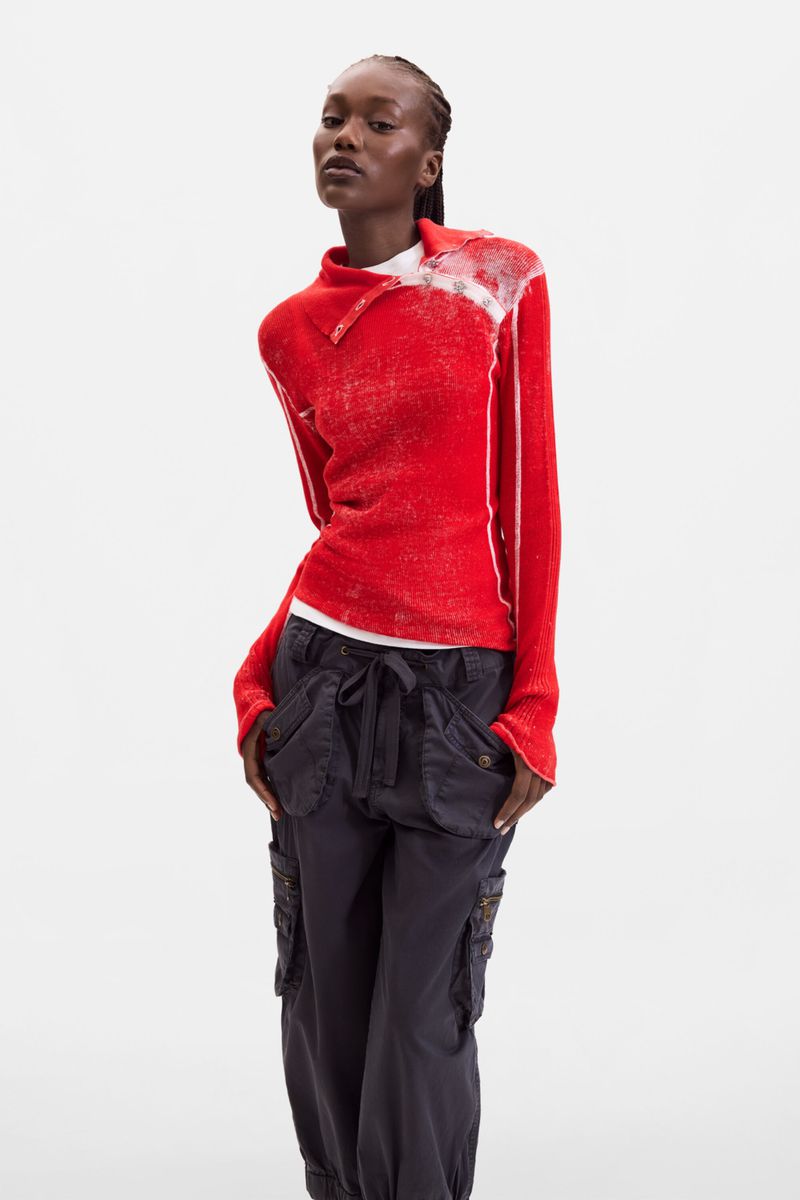 Model wearing a vibrant red long-sleeve knit top and dark utility cargo pants against a white studio background.