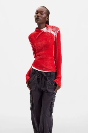 Model wearing a vibrant red long-sleeve knit top and dark utility cargo pants against a white studio background.