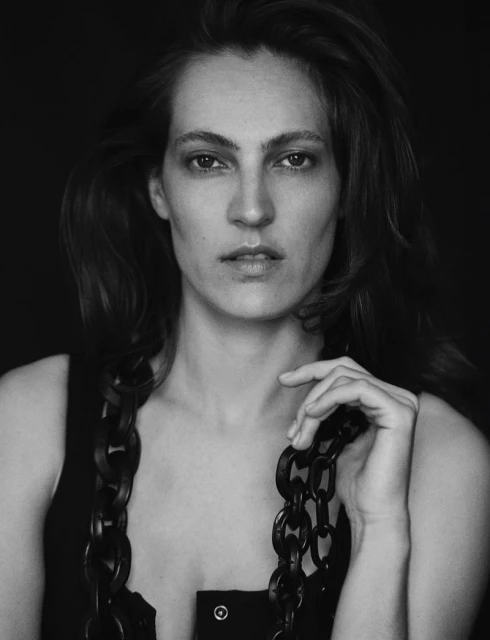 Monochromatic portrait of a woman with long hair holding a black chain, set against a dark background, captured in a close-up shot.