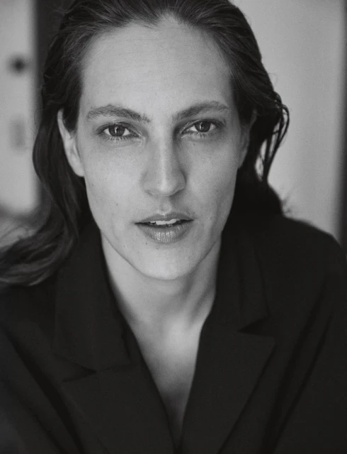 Headshot portrait of an adult woman with fair skin and dark hair wearing a black jacket against an indoor background in black and white.