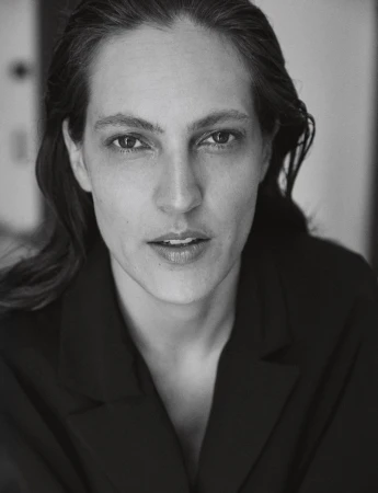 Headshot portrait of an adult woman with fair skin and dark hair wearing a black jacket against an indoor background in black and white.